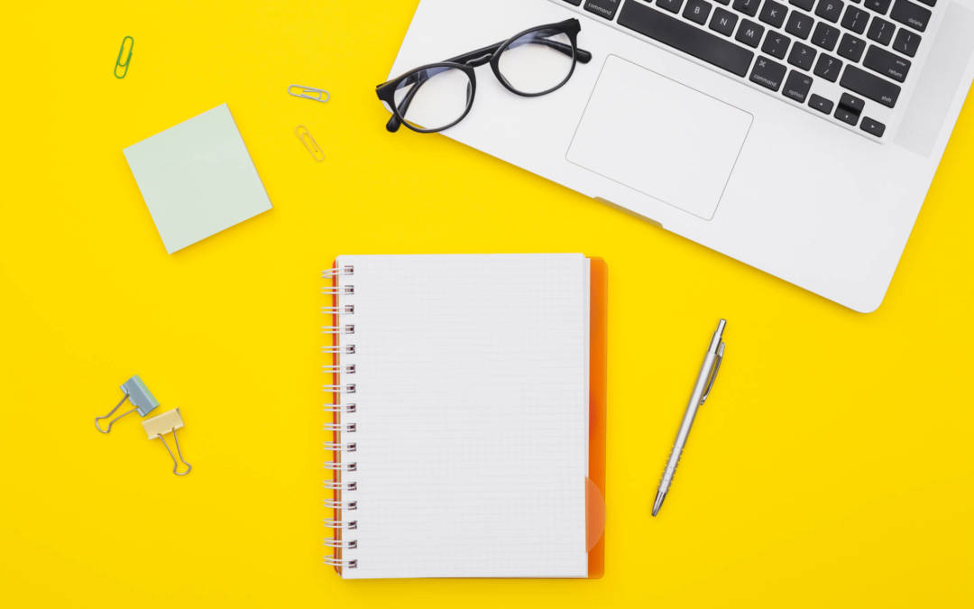 un clavier d'ordinateur, un carnet de notes, des lunettes, un stylo, le tout sur un fond jaune soleil