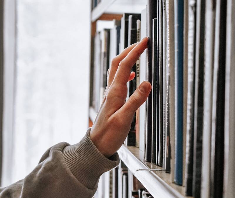 main recherchant un livre sur une étagère